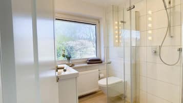 A modern bathroom with a glass shower enclosure, a toilet, and a window with a view of trees.