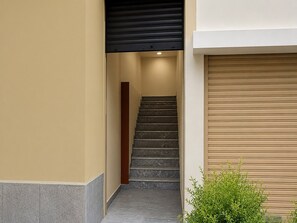 A staircase leading to an upper floor, with a closed garage door on the right and a small green plant at the bottom. - Deluxe With Balcony James Vasundhara Guest House (Hyderabad)