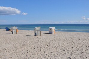 A beach with three white beach chairs and a blue lounge chair. - House El Mar, Apartment E "Brode Huus" (Großenbrode)