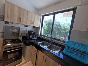 A kitchen with a gas stove, an electric microwave, a sink, and cabinets. - Untold Stays Nyali Apartment (Mombasa)