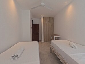 Een kamer met twee bedden, een plafondventilator, een kledingkast en een klein tafeltje.