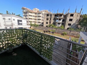Een woongebied met meerlaagsgebouwen, een balkon begroeid met klimplanten en een heldere lucht.