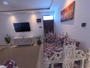 A living room with a flat-screen TV, a patterned sofa, decorative pillows, a white cabinet, and a painting on the wall. - Untold Stays Nyali Apartment (Mombasa)