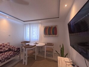 Een moderne woonkamer met een bank, stoelen, een eettafel en een grote flatscreen televisie aan de muur.