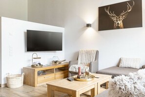 A modern living room with a flat-screen TV, a wooden coffee table, a grey sofa, and a wall-mounted artwork of a deer. - Superior Holiday Home # 5C with Sauna (Uttendorf)
