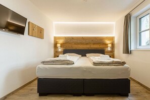 Een moderne slaapkamer met een groot bed, een houten hoofdeinde en een flatscreen televisie aan de muur.