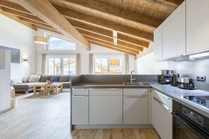 A modern kitchen with white cabinets, a wooden ceiling, and a dining area with a sofa and table. - Superior Holiday Home # 5C with Sauna (Uttendorf)