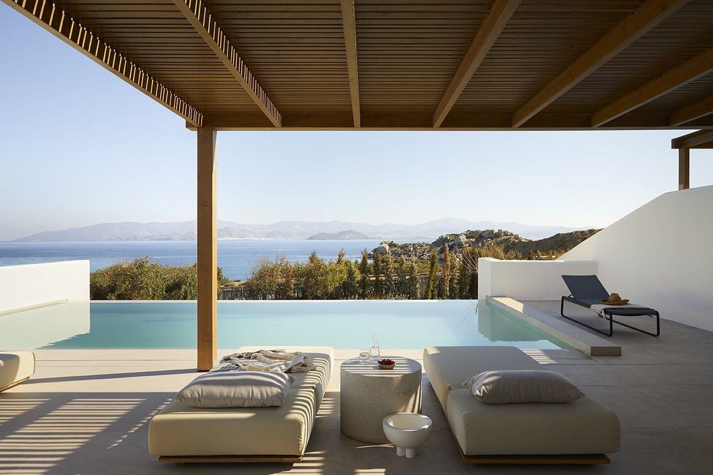 A modern outdoor lounge area with a pool, seating, and a view of the sea and mountains.