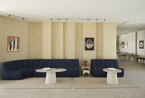 A modern living room with a large dark blue sectional sofa, two white side tables, and a neutral color palette. - Parocks Luxury Hotel and Spa (Paros)