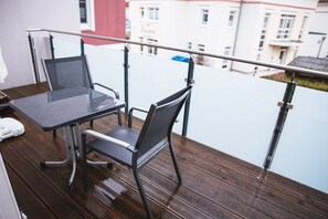 Ein Balkon mit Tisch und Stühlen, der auf ein Gebäude mit roter Fassade blickt.