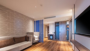 A modern living room with a sofa, a television, and a kitchen area in the background. - Holiday Inn Express Huludao Seaview an IHG Hotel (Huludao)