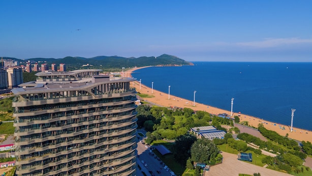 A high-rise hotel with a curved facade overlooking a beach and the sea. - Holiday Inn Express Huludao Seaview an IHG Hotel (Huludao)