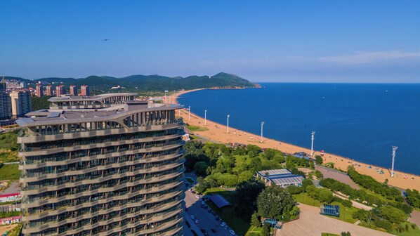Un hotel moderno de gran altura con fachada curva que domina una playa y el mar.