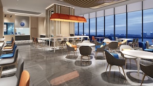 A modern dining area with tables and chairs, a large window with a city view, and a unique ceiling design. - Holiday Inn Express Huludao Seaview an IHG Hotel (Huludao)