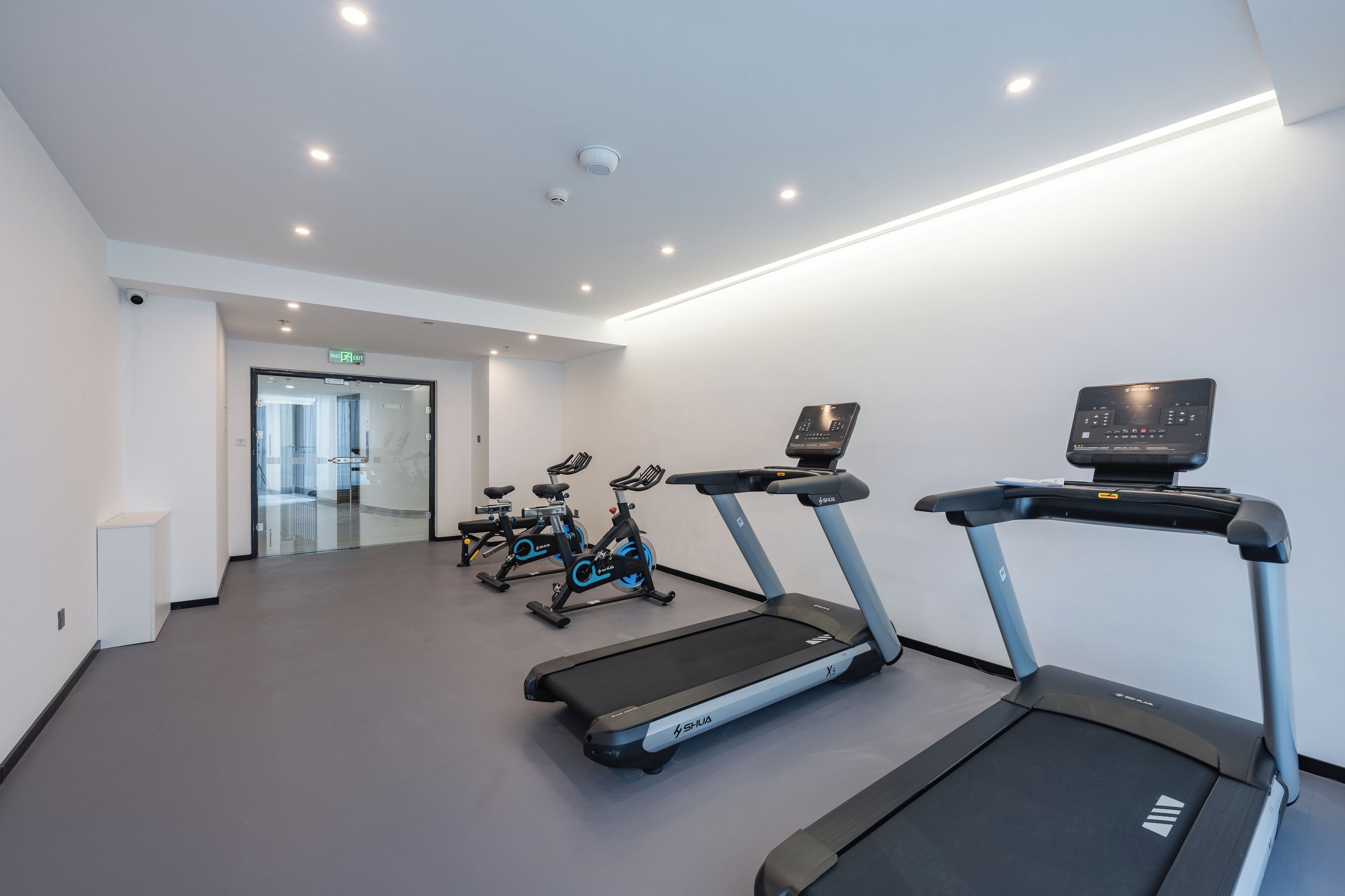 Ein Fitnessstudio mit Laufbändern, Ergometer und einem an der Wand montierten Bildschirm.