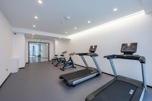 Un gimnasio con cintas de correr, bicicletas estáticas y una pantalla montada en la pared.