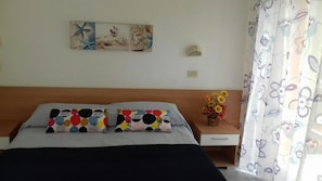 Et soveværelse med en seng, to puder, et natbord med en vase blomster, en vægmonteret lampe og et maleri.