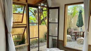 Une chambre dotée d’un grand lit, d’une porte-fenêtre coulissante donnant sur un espace extérieur avec une table et des chaises, et offrant une vue sur la verdure.