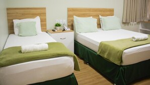 A hotel room with two beds, each with a wooden headboard, white bedding, and green bed skirts. There is a nightstand with a phone and a small plant. - Pureza Hotel (Timon)