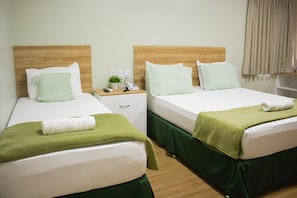 A hotel room with two beds, each with a wooden headboard, white bedding, and green bed skirts. There is a nightstand with a phone and a small plant. - Pureza Hotel (Timon)
