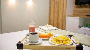 A tray with a cup of coffee, a glass of juice, a plate of scrambled eggs, and a slice of orange. - Pureza Hotel (Timon)