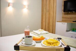 A tray with a cup of coffee, a glass of juice, a plate of scrambled eggs, and a slice of orange. - Pureza Hotel (Timon)