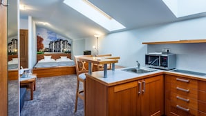 A compact hotel room with a bed, a small dining table, a kitchenette, and a skylight. - Jelinkova Vila (Velke Mezirici)