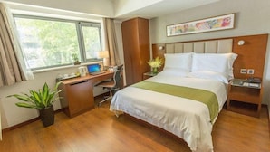 Ett hotellrum med en säng, ett skrivbord, en dator och ett fönster med gardiner.