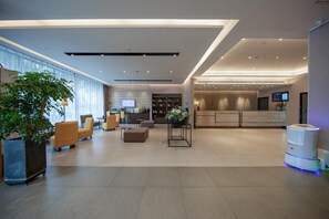 Un hall d’hôtel moderne doté d’espaces aménagés avec des sièges, d’un comptoir de réception et d’un écran de télévision.