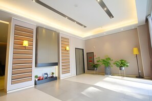 Un hall d’hôtel moderne au design épuré et minimaliste, comprenant un comptoir d’accueil, des plantes en pot et un grand miroir.