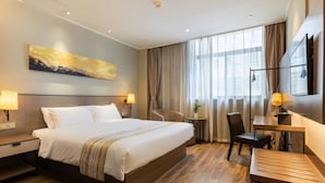 Ein Hotelzimmer mit einem großen Bett, einem Schreibtisch, einem Sessel, einem kleinen Tisch und einem Gemälde an der Wand.