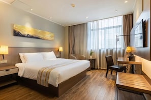 Una habitación de hotel con una cama grande, un escritorio, una silla, una mesita y un cuadro en la pared.