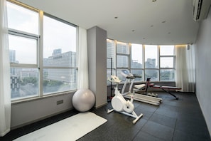 Un gimnasio moderno con equipamiento de ejercicio, ventanas amplias y vista a la ciudad.