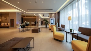 Eine moderne Hotelhalle mit Sitzbereichen, einem Empfangsbereich und einem großen Fenster, das für natürliches Licht sorgt.