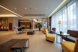 Un moderno vestíbulo de hotel con zonas de estar, un mostrador de recepción y un amplio ventanal que proporciona luz natural.