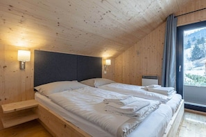 A wooden cabin room with two beds, a headboard, bedside lamps, and a window with a view. - Cabin with 1 bedroom (St. Georgen am Kreischberg)
