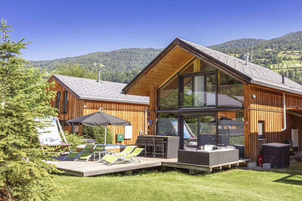 Une cabane moderne en bois dotée d’un patio, de grandes fenêtres et offrant une vue sur les collines environnantes.