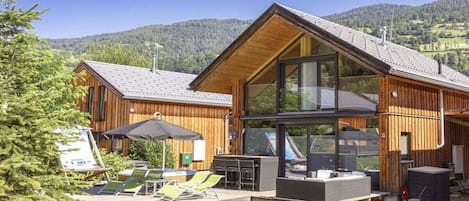 En moderne træhytte med terrasse, store vinduer og udsigt til de omkringliggende bakker.