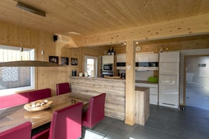 A modern kitchen with wooden walls, a dining area with red chairs, and a visible clock on the wall. - Cabin with 1 bedroom (St. Georgen am Kreischberg)