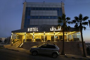 Un hotel con fachada moderna, entrada visible y un coche estacionado frente a él.