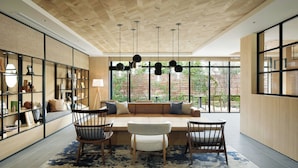 Un interno moderno con soffitto in legno, un'area salotto con divano e poltrone, e un'ampia finestra che si affaccia sul verde.