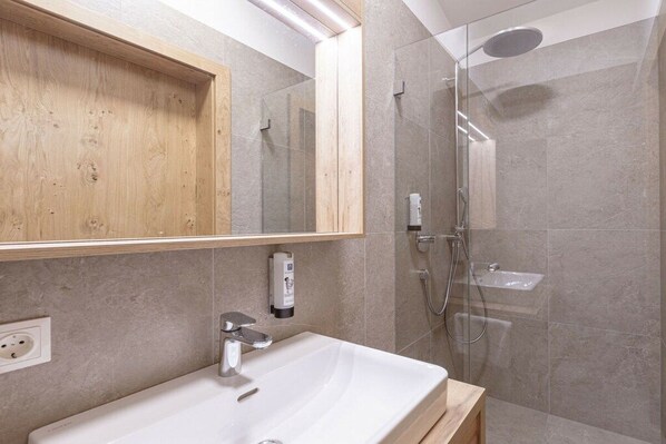 Un baño moderno con tocador de madera, un espejo grande, un lavabo blanco y una ducha con cerramiento de vidrio.