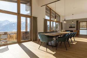 A spacious room with a large dining table, chairs, and a view of mountains through large windows. - Penthouse with 5 bedrooms (Mittersill)