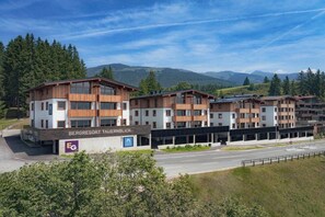 Ein mehrstöckiges Hotel mit modernem Design, das eine markante Eingangsfront und einen Blick auf die umliegenden Berge bietet.