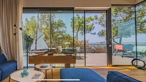A modern living room with a large sliding glass door leading to an outdoor area with a view of the sea and trees. - Villa Pyla - Côte d'Azur, 7-bedroom villa with private beach access (La Teste-de-Buch)