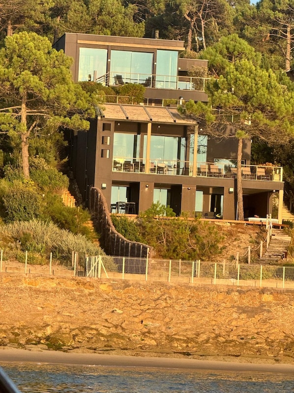 Et moderne hus med to etager, store vinduer, en balkon og en trappe op til øvre plan.