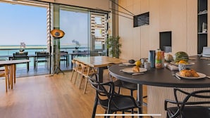 A modern kitchen with a view of the ocean, featuring a dining area with chairs and a table, a kitchen island with breakfast items, and a large window. - Villa Pyla - Côte d'Azur, 7-bedroom villa with private beach access (La Teste-de-Buch)