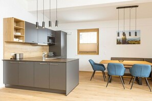 Une cuisine moderne dotée d’un îlot central, de meubles gris et d’un coin repas avec une table en bois et des chaises bleues.