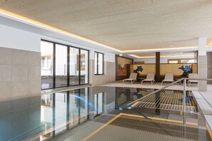 Ein moderner Poolbereich im Innenbereich mit Glaswänden, einer Sitzecke mit Stühlen und einer Treppe.
