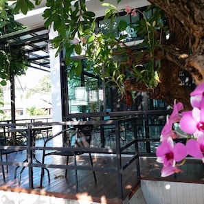 Un espacio al aire libre con mesas y sillas, rodeado de follaje y un árbol.